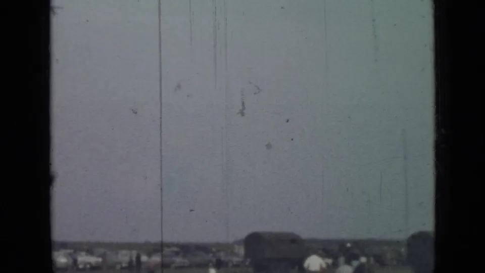 The 1967 home-movie view holds on the open field and distant cars beneath a pale, scratched sky in Saint Petersburg.