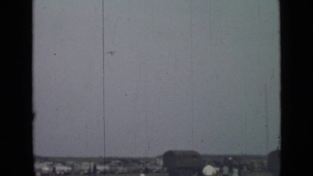 Distant airplane in a cloudy sky above a low town horizon.