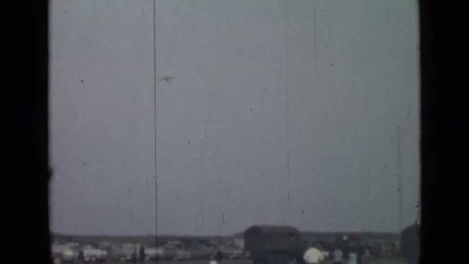 A small aircraft appears against a hazy sky over low rooftops in 1967 Saint Petersburg home-movie footage.