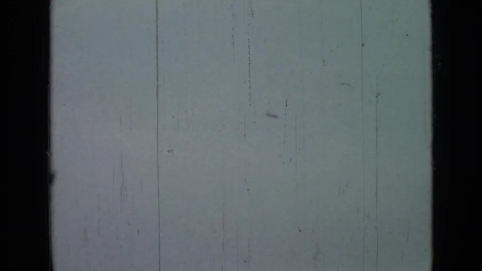 A pale overcast sky is seen through the 8mm frame, with vertical scratches and little ground detail visible.