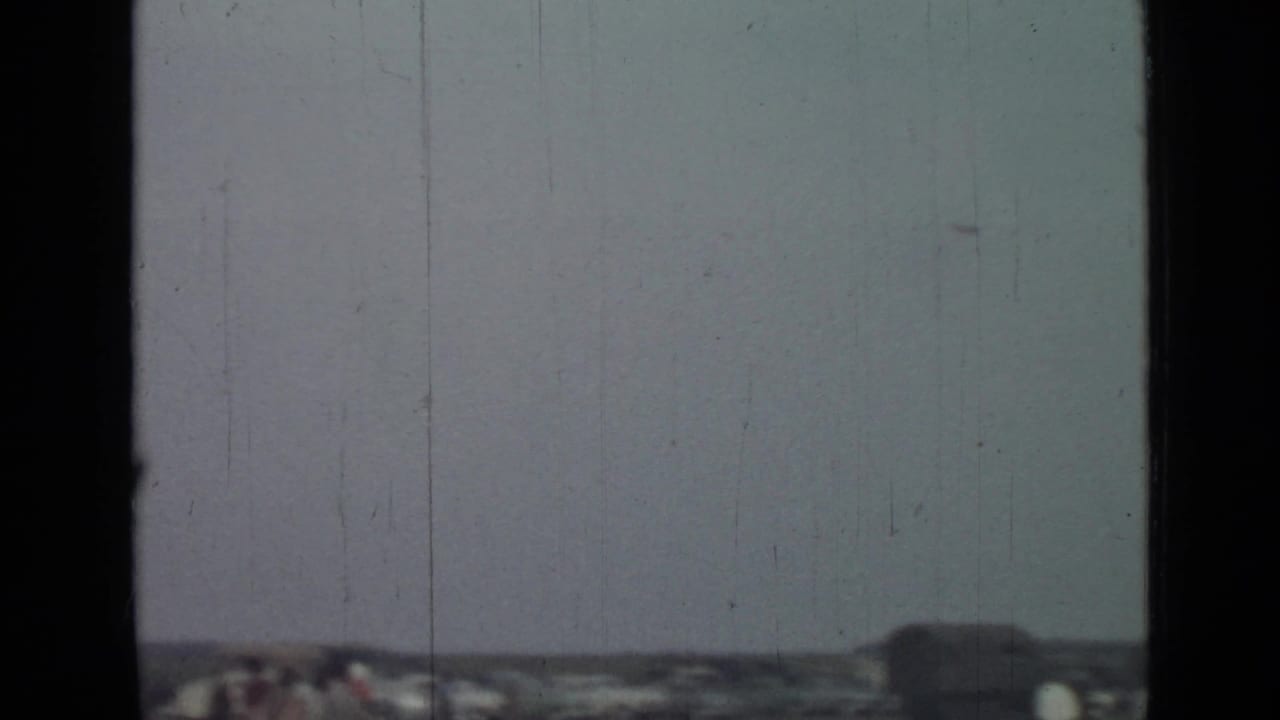 Soft 1967 8mm frame from Saint Petersburg metadata showing pale sky, low distant structures, and dark vertical gate borders.