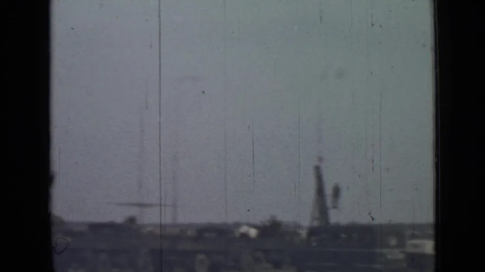 Soft 8mm view of a distant field-side area in Saint Petersburg, with low structures and a tall unclear form near the horizon.