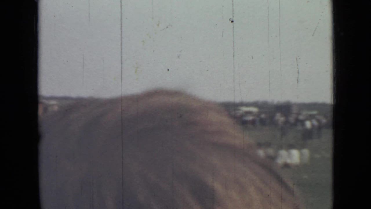 1967 Saint Petersburg home-movie view of a grassy riverbank, distant people, water, and a dark window or structural frame.