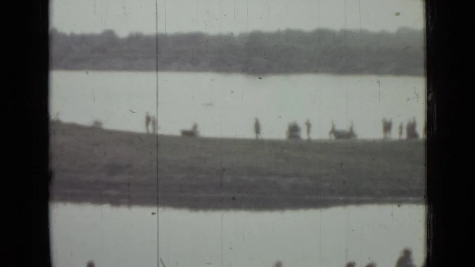 Distant 1967 Saint Petersburg riverbank scene with small groups of people on grass between water and a far tree line.