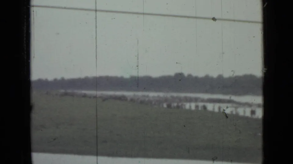 1967 8mm lakeside scene near Saint Petersburg with distant people along the water, a grassy bank, treeline, and window-frame edges.
