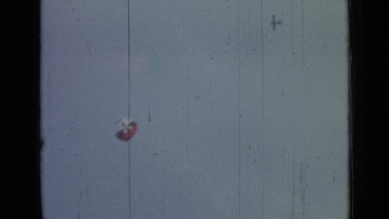 1967 8mm frame from Saint Petersburg metadata showing a distant red-and-white parachute in a pale sky with dark film borders.