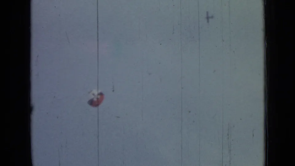 1967 8mm frame from Saint Petersburg metadata showing a distant red-and-white parachute in a pale sky with dark film borders.