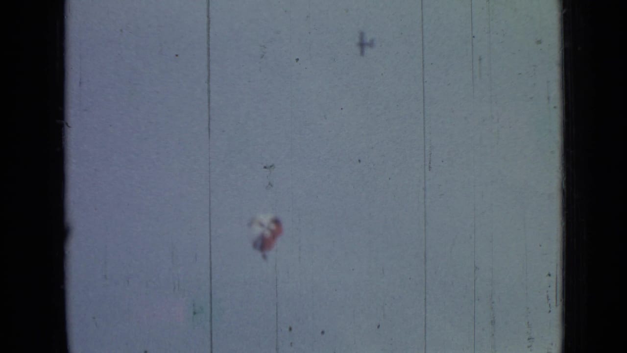 A small parachutist beneath a red-and-white canopy appears against the sky in 1967 8mm Saint Petersburg footage.