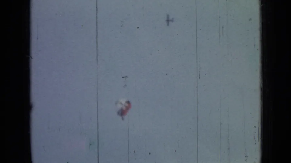 A small parachutist beneath a red-and-white canopy appears against the sky in 1967 8mm Saint Petersburg footage.