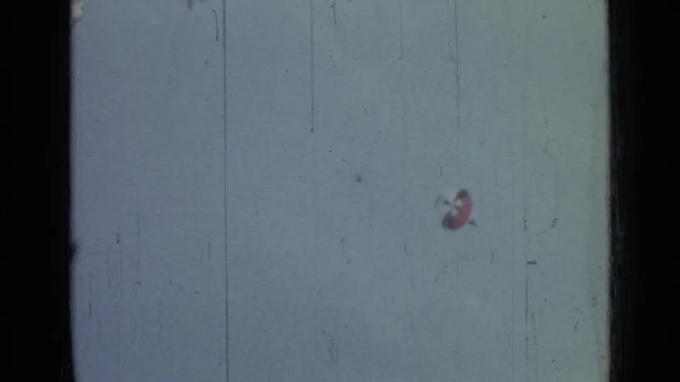 A tiny parachutist and red-and-white canopy appear in the lower sky area of this aged 8mm frame from the 1967 clip metadata.