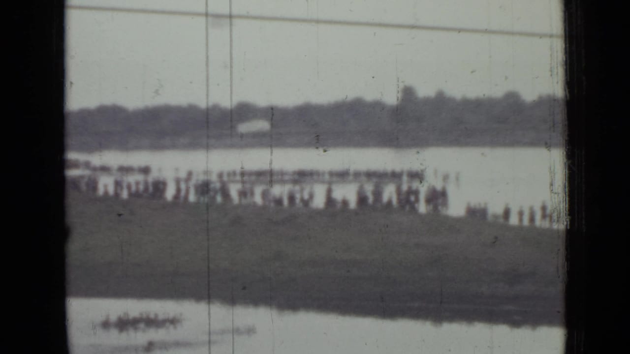Final 8mm frame shows spectators near the water in Saint Petersburg, with a small pale shape near the far bank that may be the parachute after landing.