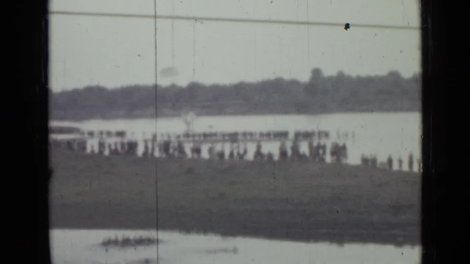Soft 1967 Saint Petersburg lakeside frame with spectators along the bank, pale water behind them, and a distant wooded shoreline.