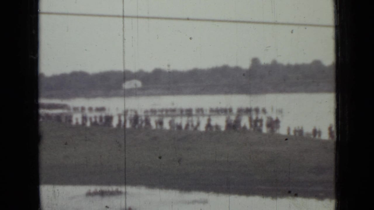 Distant 1967 8mm view of people along a Saint Petersburg shoreline with a small boat on the water and visible film wear.