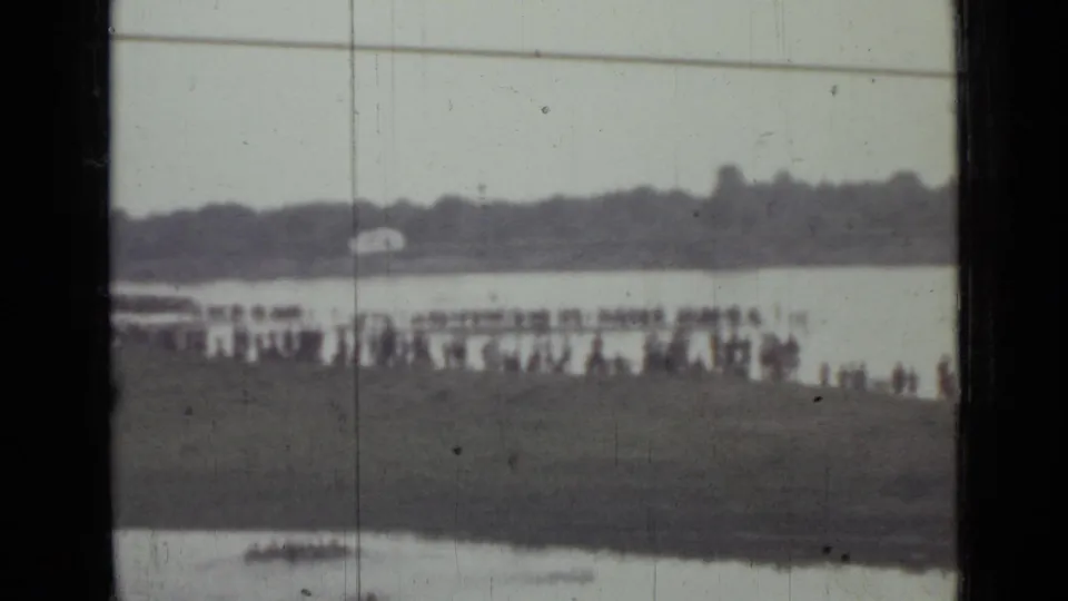 Distant 1967 8mm view of people along a Saint Petersburg shoreline with a small boat on the water and visible film wear.