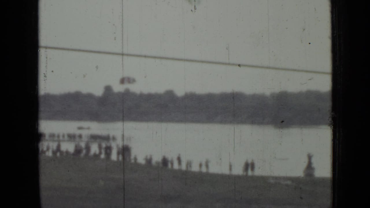Distant waterfront spectators in Saint Petersburg watch as a red parachute-like object appears over the water in 1967 footage.
