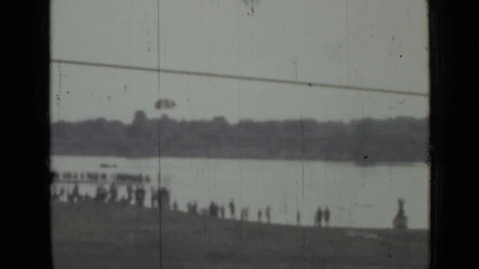 Distant waterfront spectators in Saint Petersburg watch as a red parachute-like object appears over the water in 1967 footage.