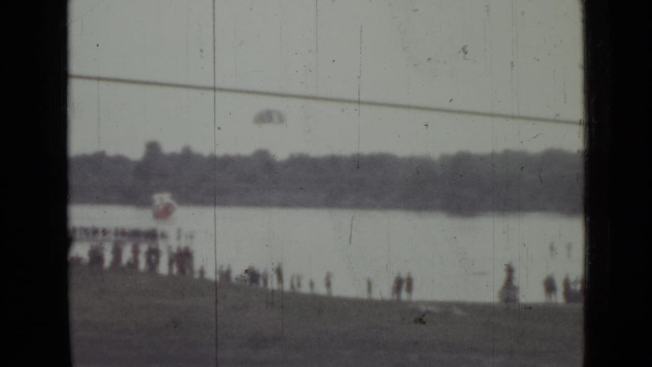 Distant 1967 Saint Petersburg river scene with a parachute over the water and people watching from the shoreline.