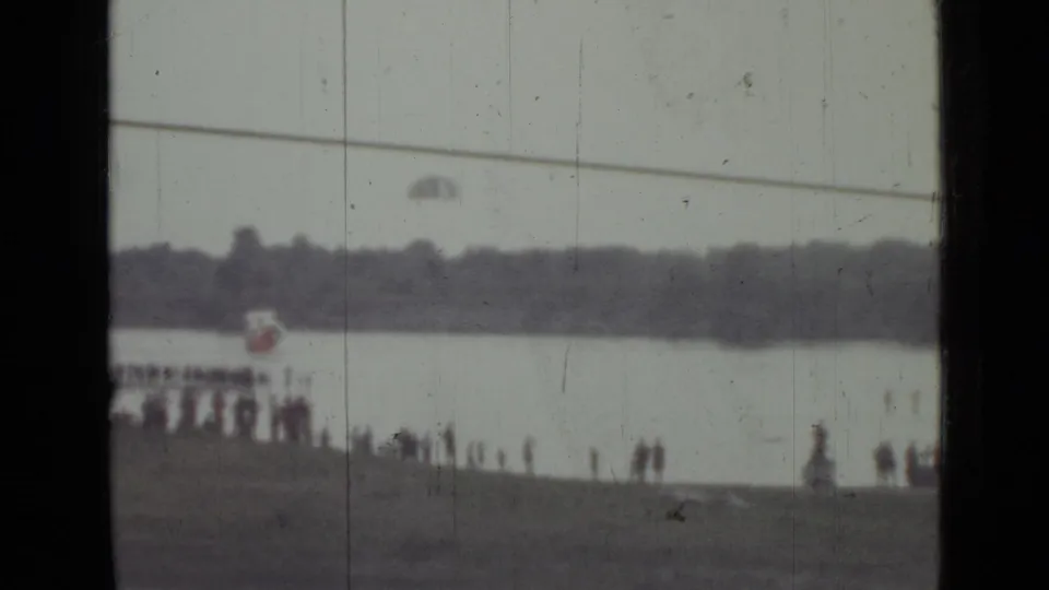 Distant 1967 Saint Petersburg river scene with a parachute over the water and people watching from the shoreline.