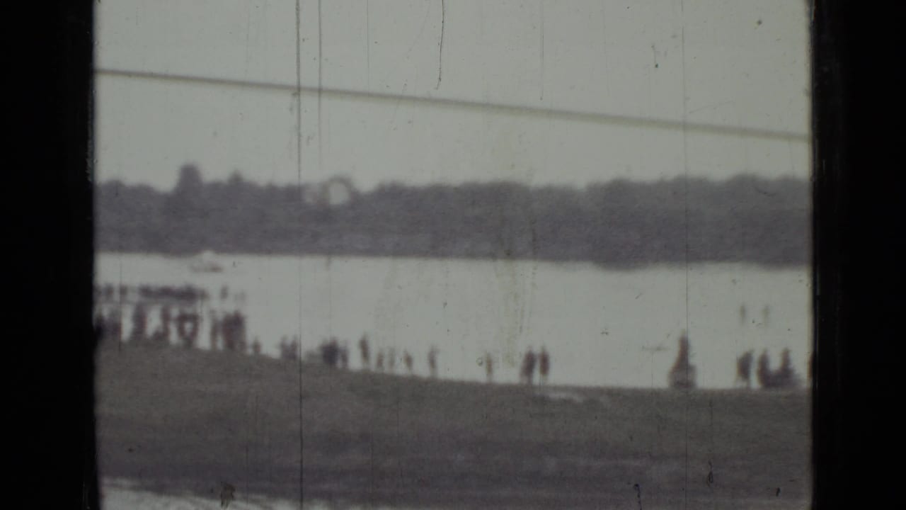 Soft 8mm frame from Saint Petersburg showing a crowd beside the river and a parachute low against the far bank.