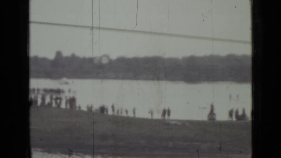 Soft 8mm frame from Saint Petersburg showing a crowd beside the river and a parachute low against the far bank.