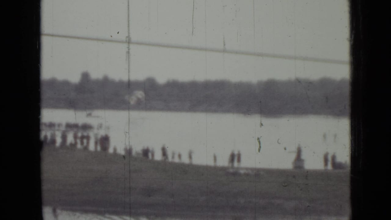 1967 Saint Petersburg home-movie frame with a second parachute descending above the river beyond a line of onlookers.