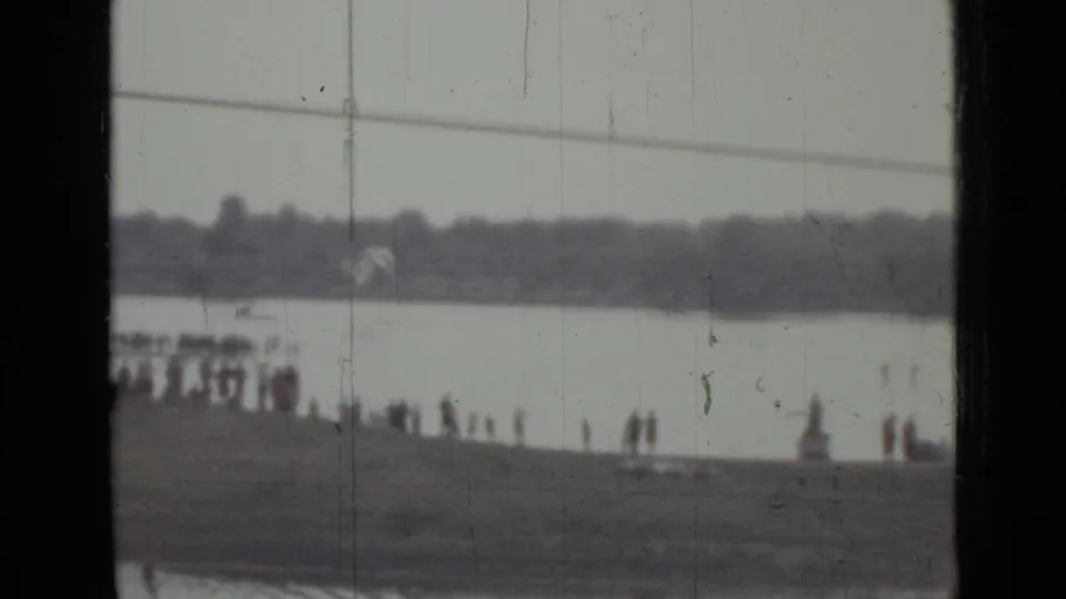 1967 Saint Petersburg home-movie frame with a second parachute descending above the river beyond a line of onlookers.