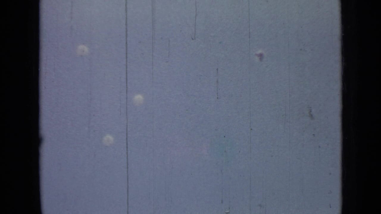 Several pale parachutes hang in a blue sky on scratched film.
