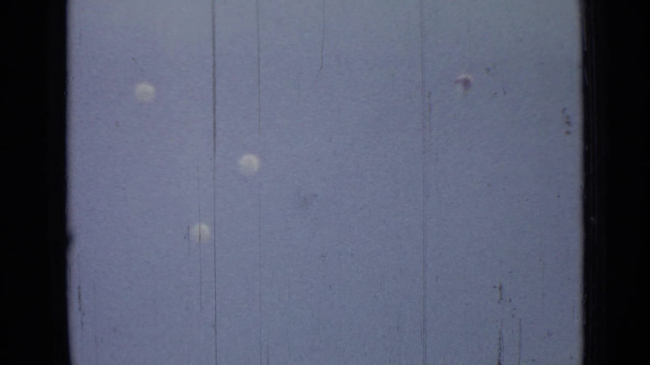 Parachutes drift downward above a faint lakeshore horizon in the Saint Petersburg 1967 home-movie scene.