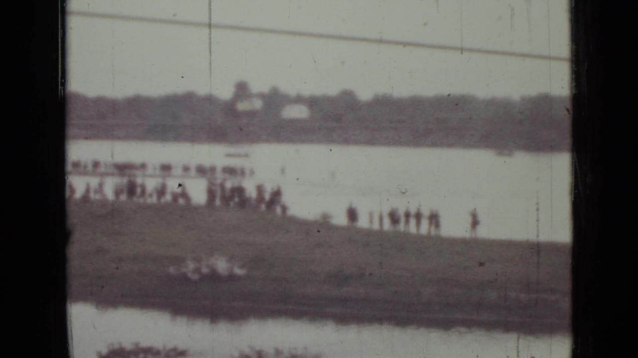 Soft 8mm frame from the Saint Petersburg clip showing small figures on the bank, pale water, and a blurred distant horizon.