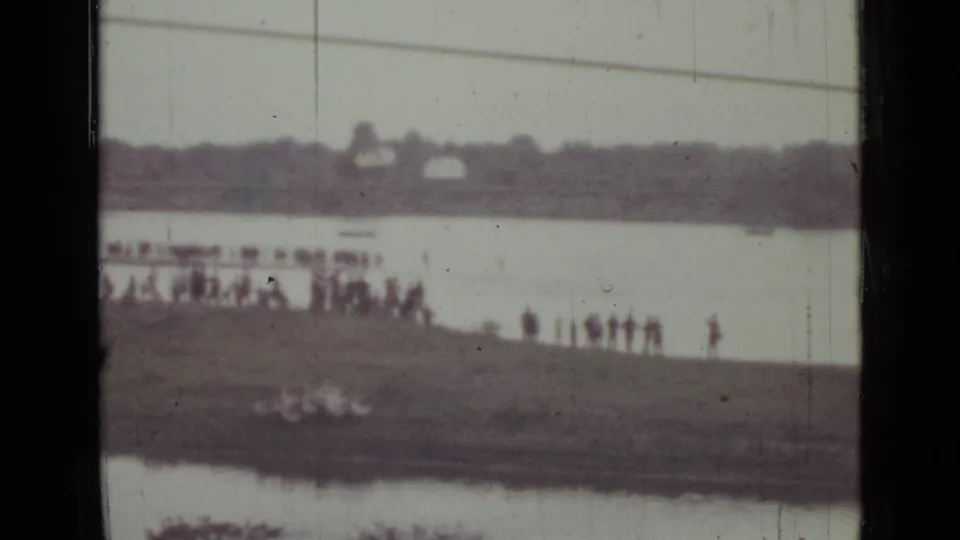 Soft 8mm frame from the Saint Petersburg clip showing small figures on the bank, pale water, and a blurred distant horizon.
