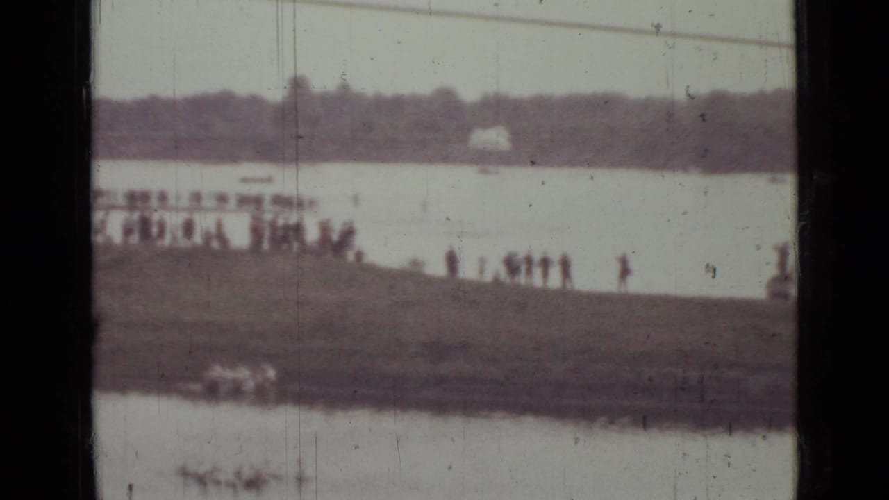 1967 Saint Petersburg 8mm frame with distant spectators on the shore and a pale parachute shape across the river.