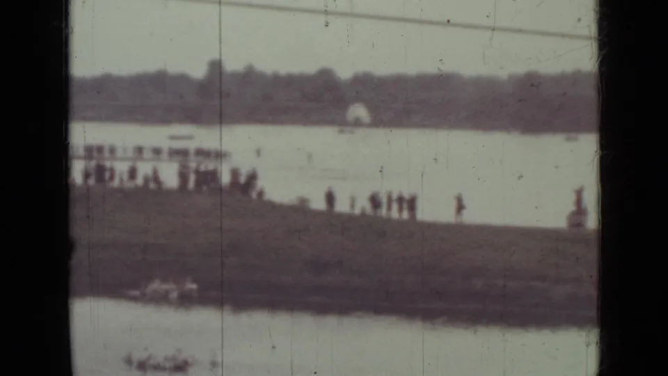 1967 Saint Petersburg home-movie frame showing a distant pier with people gathered beside calm lake water.