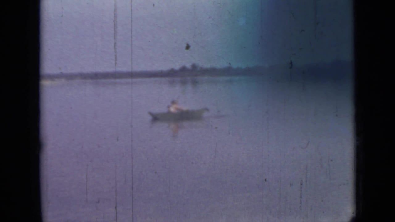 1967 Saint Petersburg home-movie frame showing a lone rower crossing a quiet lake in soft focus.