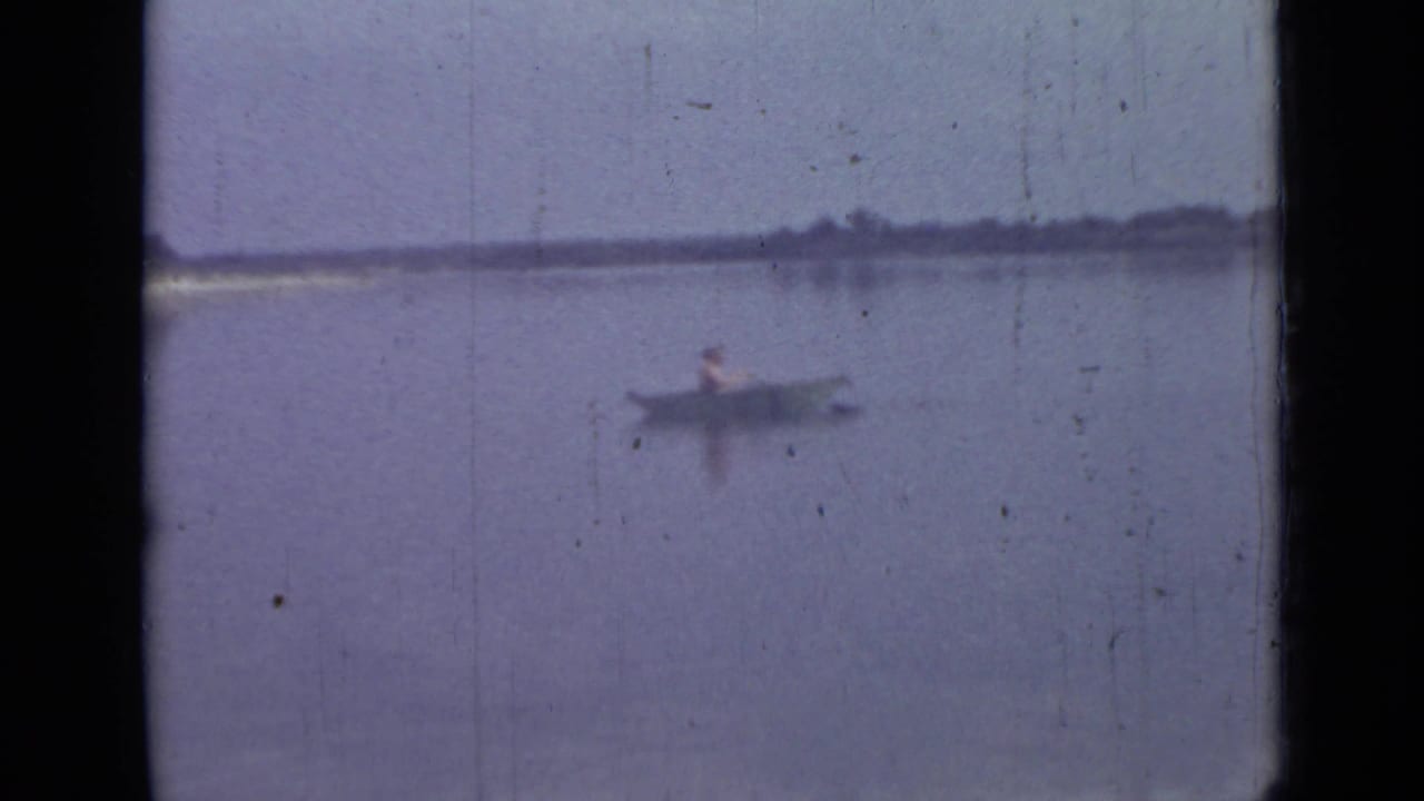 1967 Saint Petersburg lakeside frame with a lone rower in a small boat against a distant shoreline.