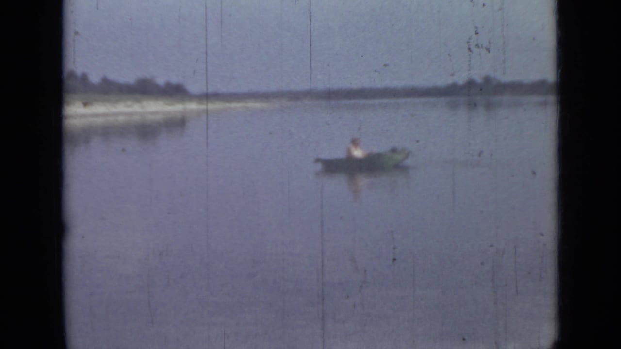 A lone canoeist appears in a small boat on calm water in 1967 Saint Petersburg footage, with a pale bank across the horizon.