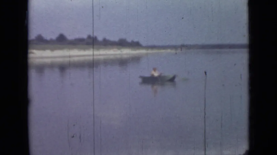 1967 8mm home-movie frame from Saint Petersburg showing one person rowing a small boat across a calm lake near a distant shore.