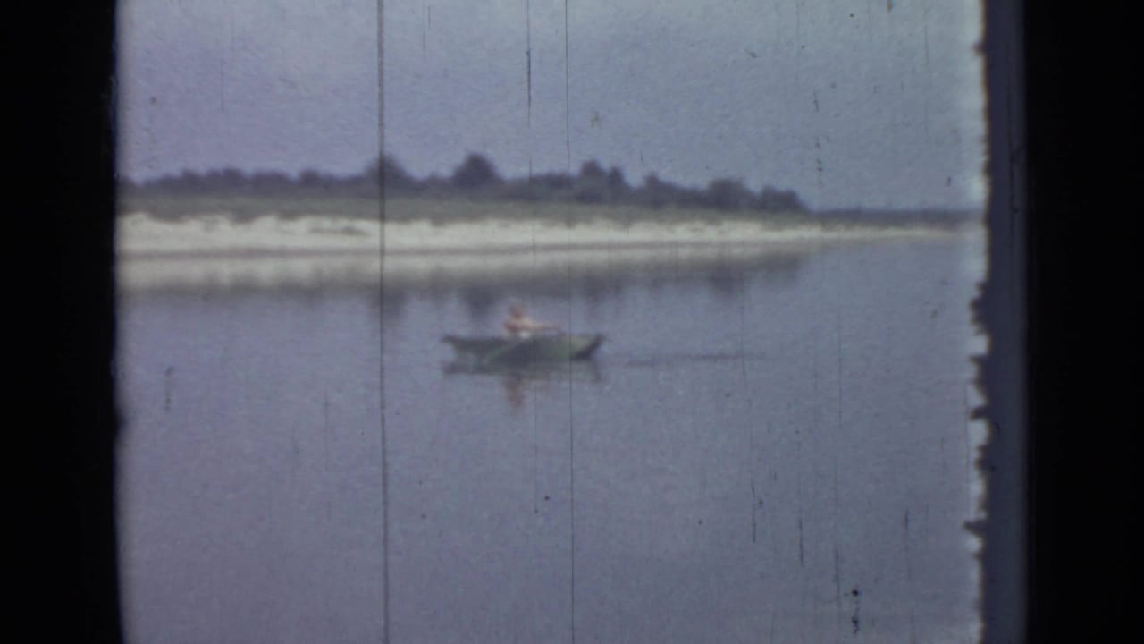 A 1967 8mm home-movie frame shows one distant person rowing on a lake near Saint Petersburg, with scratches and soft color visible.