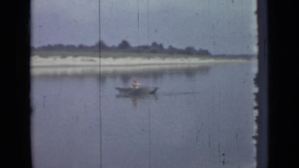 A 1967 8mm home-movie frame shows one distant person rowing on a lake near Saint Petersburg, with scratches and soft color visible.