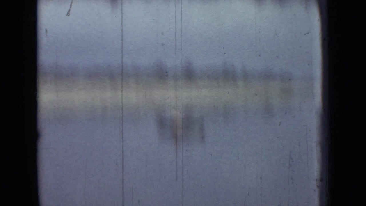Soft, hazy view across calm water with a distant shoreline and film gate edges.