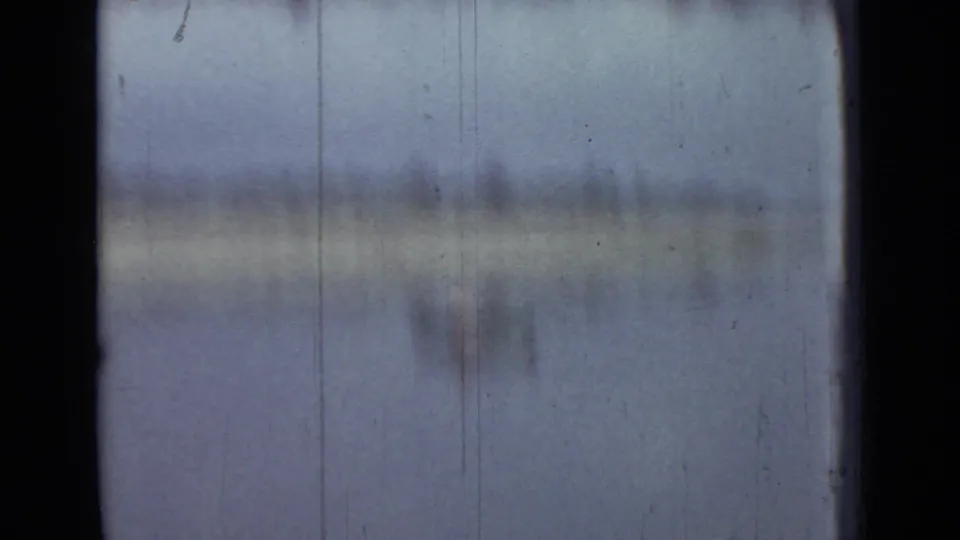 1967 8mm home-movie frame from Saint Petersburg showing calm water, a pale shoreline, low trees, and heavy soft focus.