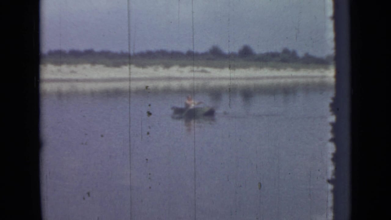 Small rowboat on calm water near a distant sandy shoreline.