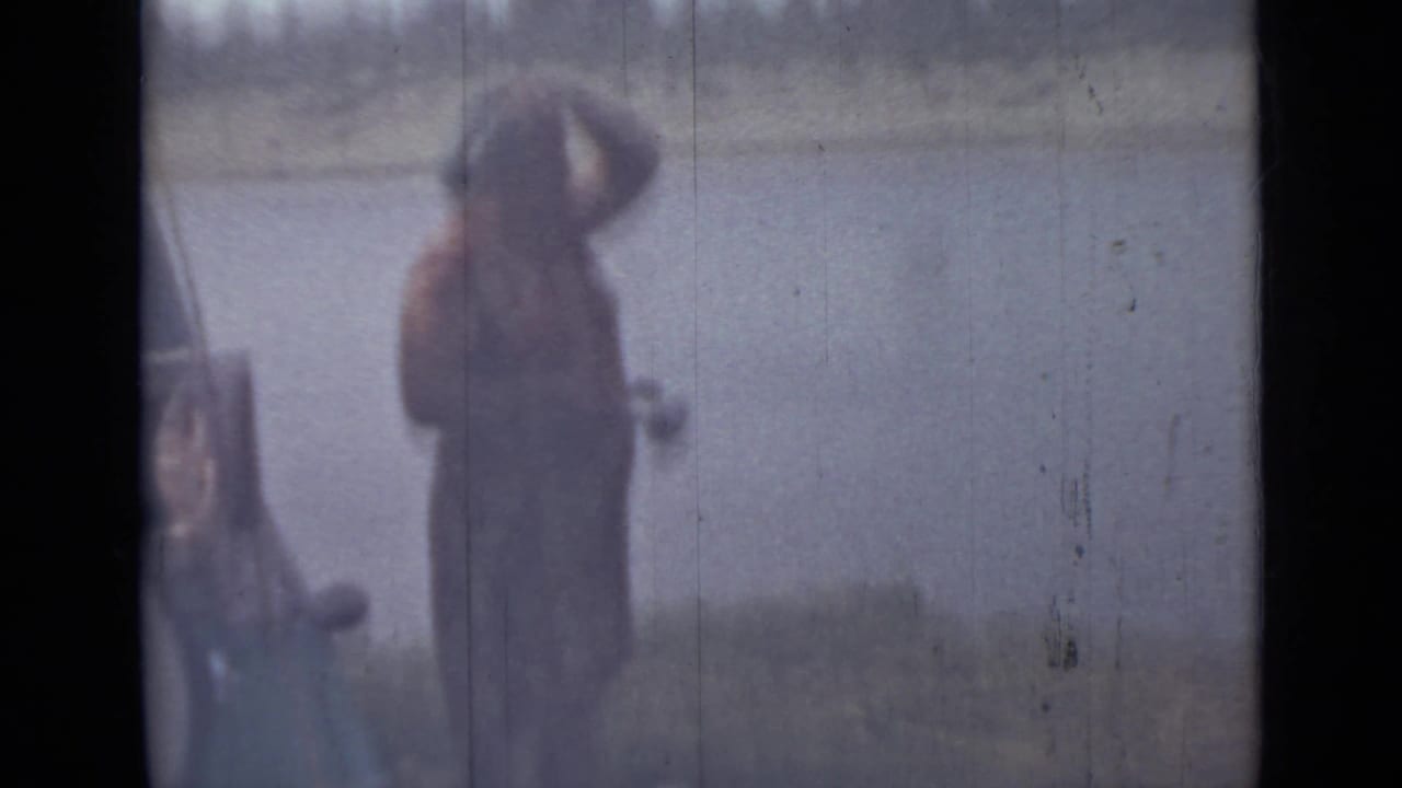 Blurred shoreline figure stands beside the water in the final 1967 Saint Petersburg home-movie frame, with the river behind them.