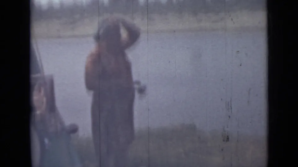 Blurred shoreline figure stands beside the water in the final 1967 Saint Petersburg home-movie frame, with the river behind them.