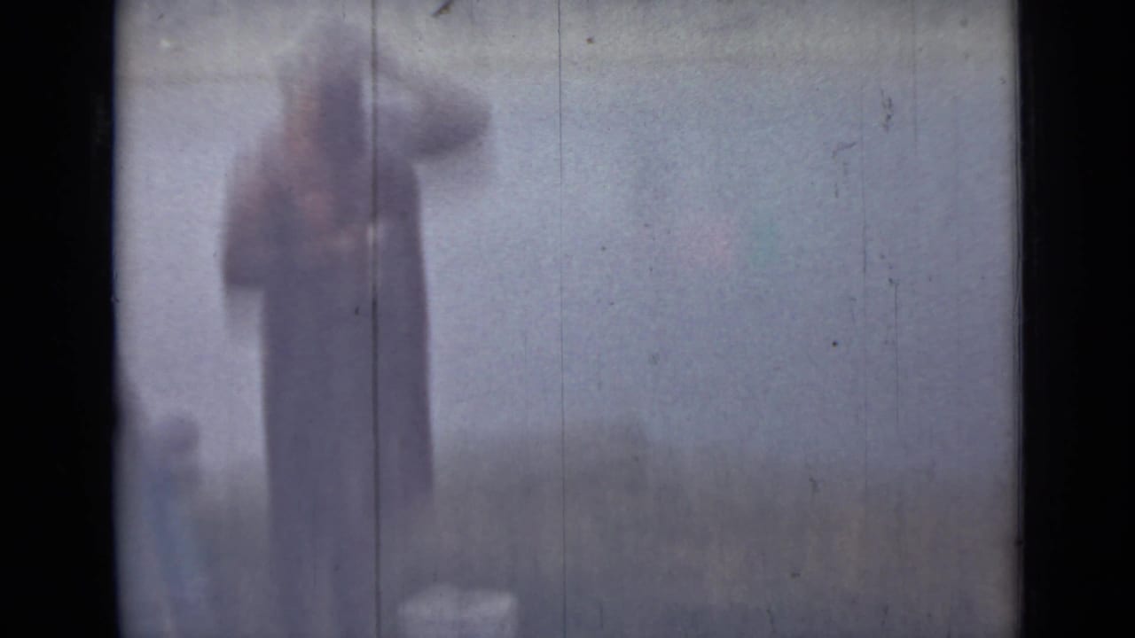 Blurred standing woman near hazy water and low riverbank vegetation.