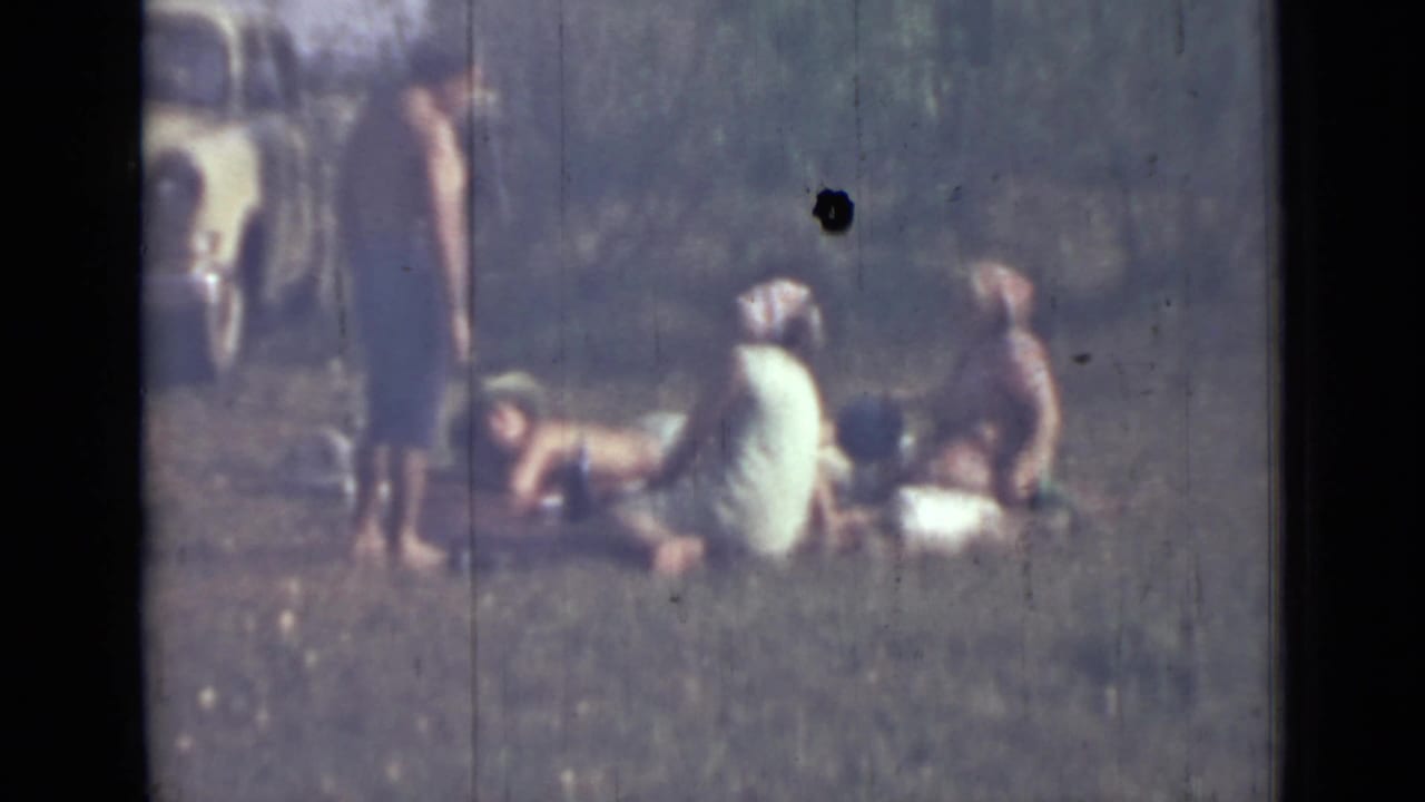People sit and recline on grass while a man stands nearby.