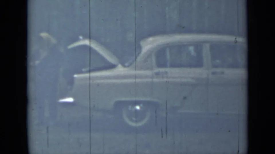 A person stands near a light-colored vintage sedan with the trunk open in the 1967 Saint Petersburg home-movie footage.
