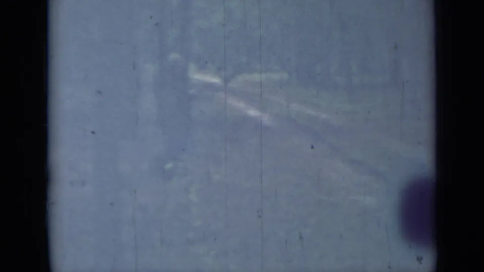 1967 home-movie still showing a dim snowy trail or wooded path, partly obscured by fading and 8mm film damage.