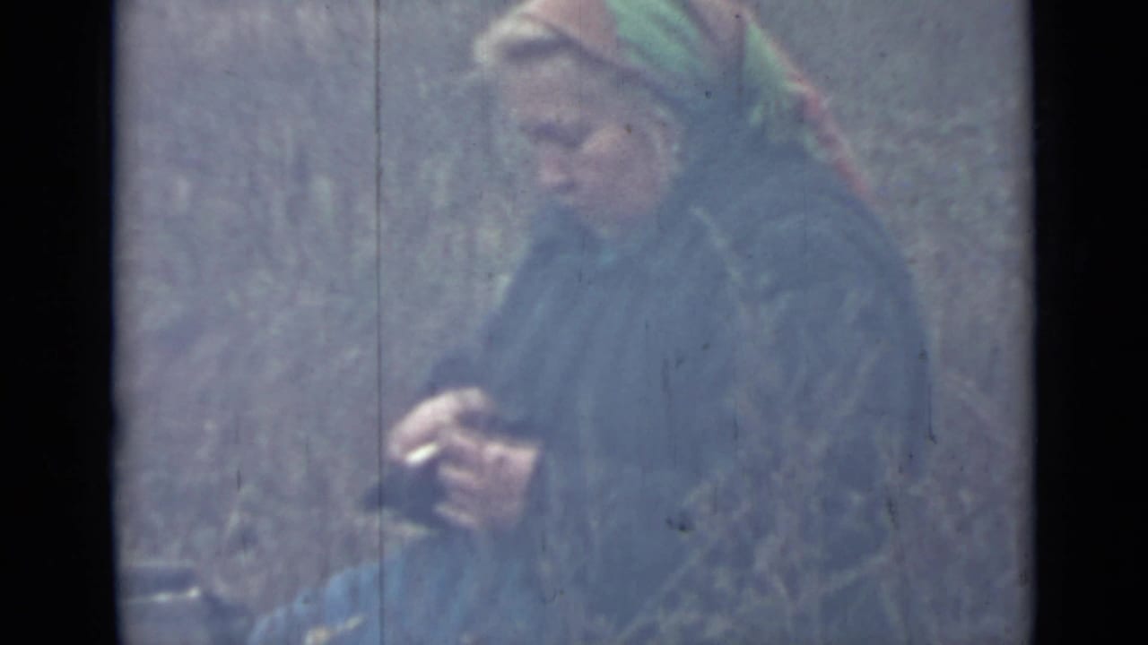 In 1967 Saint Petersburg home-movie footage, a bundled woman in a colorful headscarf holds a potato and small knife outdoors.
