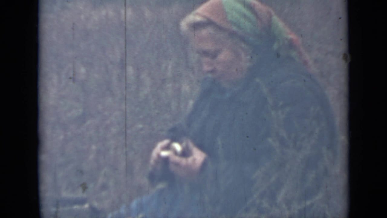 Woman in a headscarf looking down while holding a potato and knife.