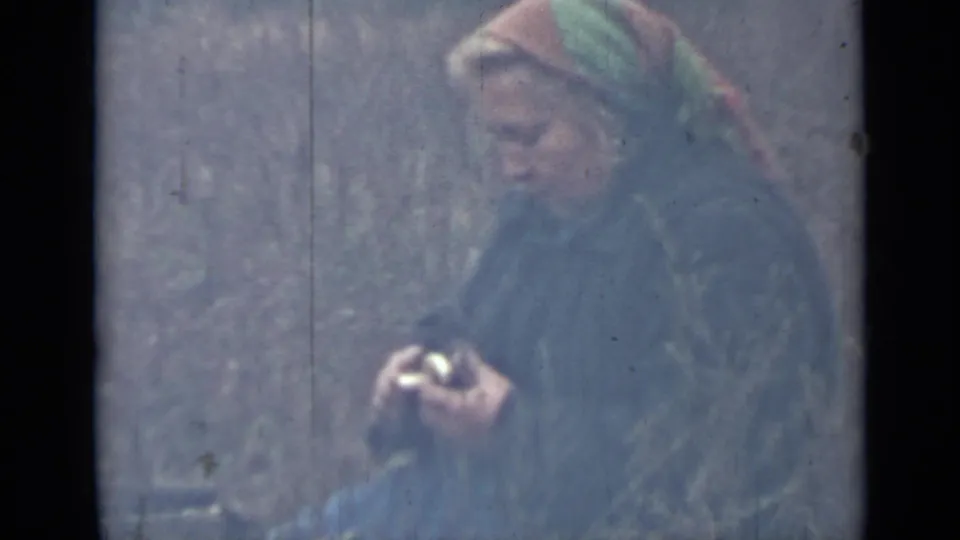 The woman looks down at her hands while peeling a potato in an outdoor Saint Petersburg setting documented on 8mm film.